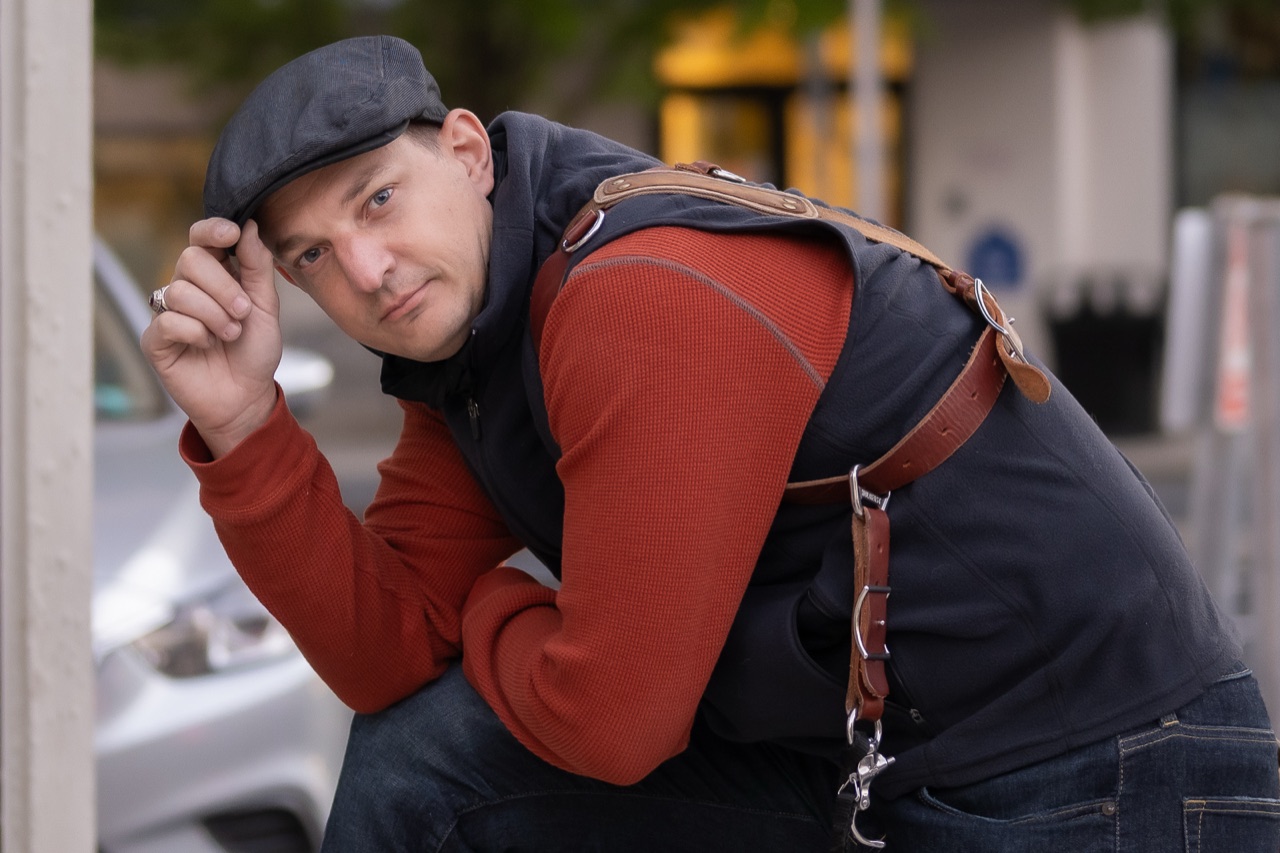 Portrait photographer in a flat cap leaning forward during a booking consultation