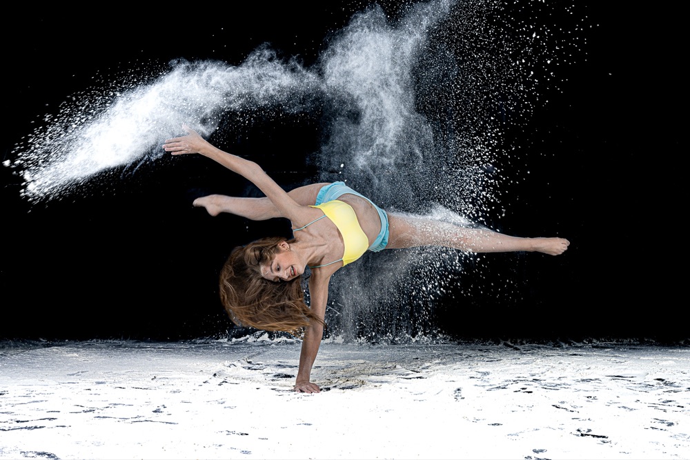 Dancer extending through a powder-filled leap against a black background