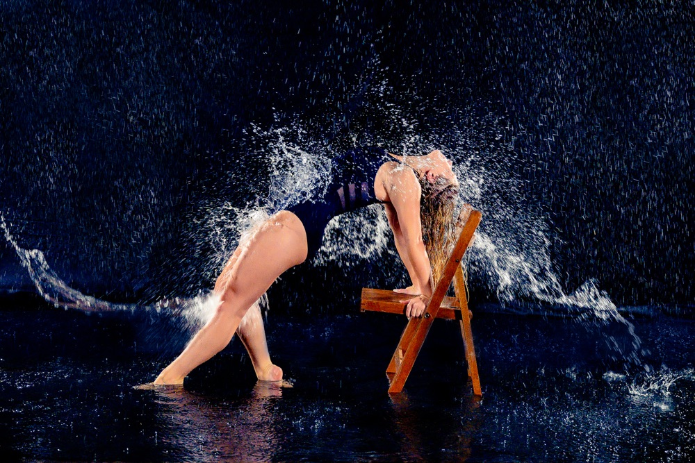 Dancer arching backward in a rain-filled creative portrait with a dark, cinematic backdrop