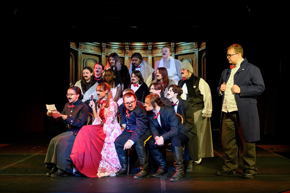 Large ensemble of performers posed on stage in period costumes